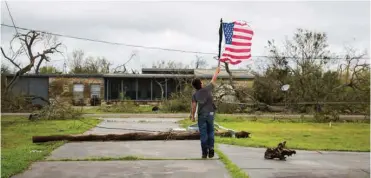  ?? Associated Press ?? LEFT: Layton Carpenter walks down an empty driveway in Bayside, Texas, holding a broken American flag that he found in the water.