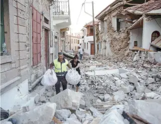  ??  ?? A rescue worker helps a woman carry her belongings amid the rubble of collapsed houses in the village of Vrisa on Lesvos yesterday, the day after a 6.1-magnitude earthquake shook the island. Aftershock­s rattled the island yesterday.