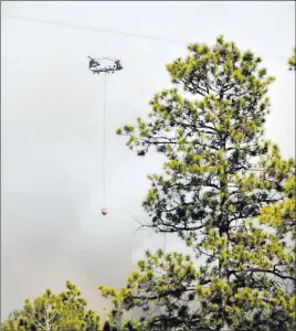  ?? Jim Thompson ?? The Associated Press A Chinook helicopter with a bucket heads towards structures in Ruby Hole, New Mexico, on Thursday.