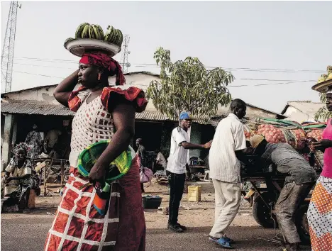  ?? PHOTOS: JANE HAHN/ THE WASHINGTON POST ?? People walk through the market in Brikama-ba Village, Gambia. Those with relatives in Europe are rich in comparison to their neighbours.