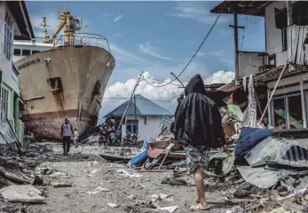 ?? FOTO: HARIANDI HAFID ?? Menschen gehen eine Straße entlang in der Nähe des Ortes, wo ein Schiff während des Tsunamis an Land gespült wurde.