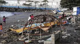  ?? ASSOCIATED PRESS ?? Residents walk beside an outrigger and playground equipment that were damaged by Typhoon Phanfone along a coastline in Ormoc city, central Philippine­s, on Thursday. The typhoon left at least 20 dead and many homeless.