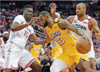  ??  ?? LeBron James (centre) of the Los Angeles Lakers tries to go past Clint Capela (right) of the Houston Rockets and P. J. Tucker during their NBA game in Houston on Saturday. The Lakers won 124-115. — AP