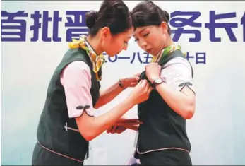  ?? YIN LIQIN / CHINA NEWS SERVICE ?? Yeh Yu-ching (left) and Huang Chia-ying, flight attendants for Spring Airlines, help each other with their nametags in Shanghai on Wednesday. The two have just been promoted to cabin crew chiefs — the first workers from Taiwan to be given the positions...
