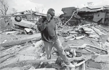  ??  ?? Anthony Brown walks Wednesday through debris from what was the house of a New Orleans East neighbour, whom he helped extricate after she was trapped inside in the aftermath of Tuesday’s powerful tornado.