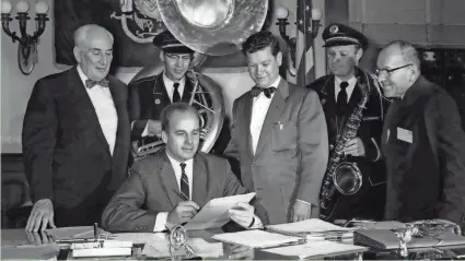  ??  ?? Gov. Gaylord Nelson (center) signs a bill making “On, Wisconsin” the state’s official song on July 7, 1959. Looking on are state Sen. Leo O’Brien (from left); William Schoeverli­ng, sousaphone player with the Oconomowoc American Legion band; state Rep....