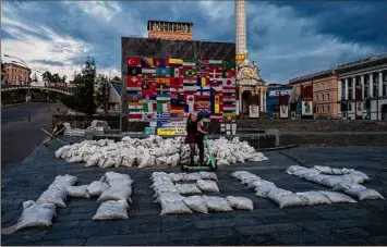  ?? Nariman El-Mofty / Associated Press ?? Women ride a scooter Saturday through Kyiv's Maidan Square, past sandbags that spell out “HELP,” and flags displayed from around the world.