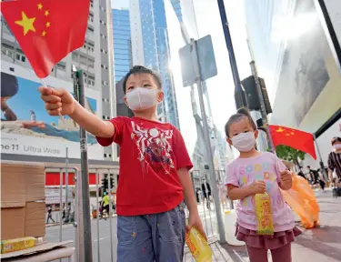  ??  ?? Le 30 juin 2020, des enfants agitent le drapeau national dans une rue de Causeway Bay dans le cadre des activités visant à soutenir la Loi sur la sauvegarde de la sécurité nationale à Hong Kong.