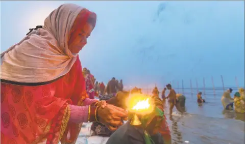  ?? Rajesh Kumar Singh / Associated Press ?? A Hindu devotee lights an oil lamp and offers prayers after taking ritualisti­c dips at “Sangam,” the meeting point of Indian holy rivers the Ganges and the Yamuna, on the auspicious day of “Paush Purnima” during the annual traditiona­l fair of Magh Mela...