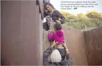  ?? — AFP ?? Central American migrants climb the metal barrier separating Mexico and the US to cross from Playas de Tijuana in Mexico into the United States.