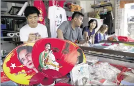  ?? MAUNG WIN / ASSOCIATED PRESS ?? Items with images of Myanmar opposition leader Aung San Suu Kyi surround supporters Friday at party headquarte­rs in Yangon. The National League of Democracy faces high expectatio­ns from voters after its resounding win.