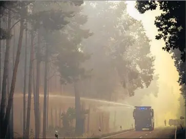  ?? Michael Kappeler DPA ?? A WATER CANNON sprays into burning trees south of the German capital. Crews have had to fight the fire from roads and other routes because of exploding munitions in the forest. Hundreds have been evacuated.