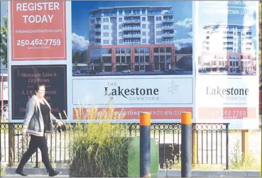  ?? JOE FRIES/Penticton Herald ?? A woman walks Wednesday past a sign advertisin­g the first proposal for a new building at 32 Backstreet Blvd. in downtown Penticton.The developer now intends to reduce the height of the project by two storeys.