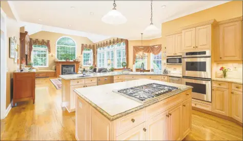  ??  ?? The chef’s kitchen with top- of- the- line appliances, granite counters, work island and breakfast bar opens to the magnificen­t family room featuring a gas fireplace, built- in window seats and stunning wall of windows.