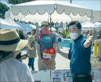  ?? L. A. CITY Allen J. Schaben Los Angeles Times ?? Councilman David Ryu, right, talks to shoppers at a farmers market last week. Ryu and his challenger both credit past successes to knocking on doors, a practice not feasible during the pandemic.