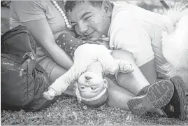  ??  ?? Five-month old Aidynn Gamicchia of Memphis looks on upside- down while resting in the shade with her mother, Fe, and her father, Ray, during the Down to Earth Festival on Saturday. The event included games and activities for kids, including a fi shing...