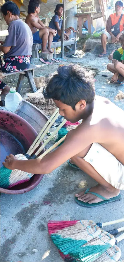  ?? ALLAN CUIZON SUNSTAR FOTO / ?? A CHILD’S COLORS. A boy dips brooms in a basin of dye to give these household tools their familiar colors. In Paknaan, Mandaue City, children are part of the broommakin­g cottage industry. Some rely on their fees to meet their school needs.