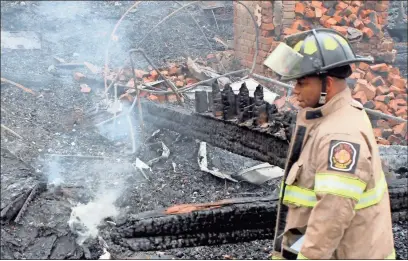  ?? Doug Walker ?? Fire investigat­or Brenton Whatley checks over the still smoldering remains of a home at 50 Biddy Road which was destroyed Thursday night.