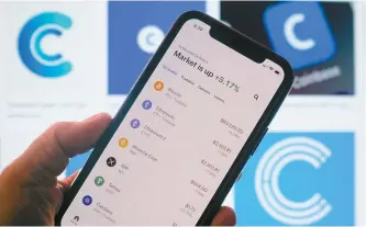  ?? AFP-Yonhap ?? The Coinbase logo is seen in the background as a person checks cryptocurr­encies prizes on a smartphone in Los Angeles, April 13.