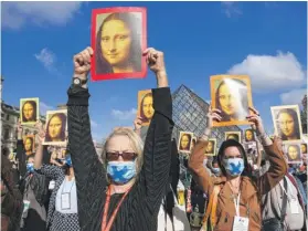  ?? PASCAL LE SEGRETAIN/GETTY IMAGES ?? Visitors hold images of the Mona Lisa outside Paris’ Louvre museum on Monday as it reopened after a 16-week closure.