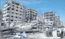  ?? HASSAN AMMAR — THE ASSOCIATED PRESS ?? People stand in front of damaged buildings Monday in the town of Douma, the site of a suspected chemical weapons attack near Damascus, Syria.