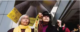  ?? —AFP ?? HONG KONG: Two women hold an umbrella as they protest in support of elected pro-democracy lawmakers Edward Yiu, ‘Long Hair’ Leung Kwok-hung, Nathan Law, and Lau Siu-lai outside the High Court before they face a judicial review into whether they should...