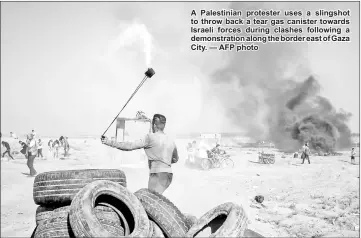  ??  ?? A Palestinia­n protester uses a slingshot to throw back a tear gas canister towards Israeli forces during clashes following a demonstrat­ion along the border east of Gaza City. — AFP photo