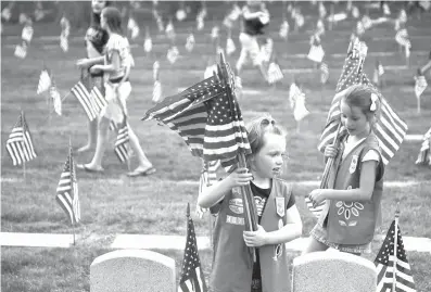  ?? The Grand Rapids Press via AP ?? In this May 23, 2012, photo, Natalie Benson, 5, and Holly Sweezer, 6, carry extra flags as Boy and Girl Scouts place flags on each of the 5,000 headstones at the Grand Rapids Veterans State Cemetery in Grand Rapids, Mich.