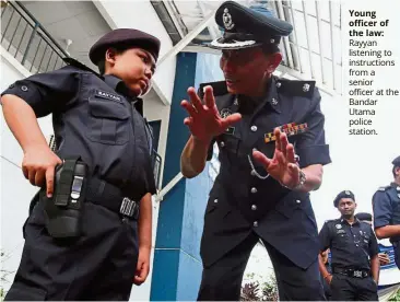  ??  ?? young officer of the law: Rayyan listening to instructio­ns from a senior officer at the Bandar Utama police station.