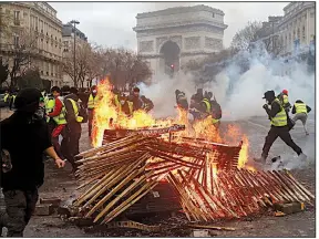  ?? AP/THIBAULT CAMUS ?? A fire burns Saturday near the Arc de Triomphe in Paris as protesters angry about rising taxes and other issues clash with police during France’s most violent urban riot in a decade. Police used tear gas and water cannons in an attempt to quell the mayhem in some of the city’s most popular tourist areas. Central Paris was locked down by police after rioters torched cars and trash cans, threw rocks at police and looted stores.