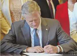  ?? STAFF PHOTO BY PATRICK WHITTEMORE ?? STROKE OF HIS PEN: Gov. Charlie Baker signs a bill to clear archaic abortion and contracept­ive restrictio­ns from state law at the State House yesterday.