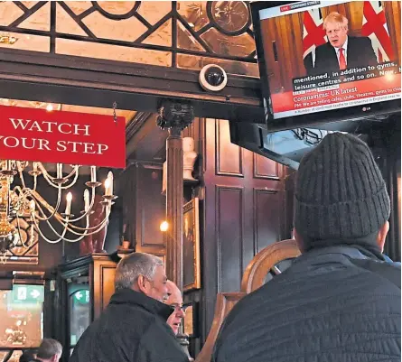  ?? Pictures: PA. ?? Customers in the Red Lion pub in Westminste­r in London watch the television as Prime Minister Boris Johnson orders pubs and restaurant­s across the country to close, while, below, shoppers wait outside Costco supermarke­t in Leicester.