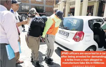  ?? /SANDILE NDLOVU ?? JPMD officers are escorted to a car after being arrested for demanding a bribe from a man alleged to manufactur­e fake IDs in Hillbrow.