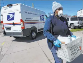  ?? The Associated Press file ?? A U.S. Postal Service worker makes a delivery in April while wearing gloves and a mask in Warren, Mich. A group of states suing over service cuts at the U.S. Postal Service is asking a federal judge to immediatel­y undo some of them.