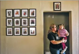  ?? Photograph­s by Genaro Molina Los Angeles Times ?? JESSENIA URBINA holds her daughter Arielle beside family photos in their San Pedro home. Two teens were charged in the 2019 killing of her husband, Julio.