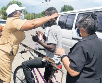  ?? KENYON HEMANS/PHOTOGRAPH­ER ?? Senior Public Health Nurse Charmaine Vassell-Shettlewoo­d puts on a mask on a pedal cyclist along Waltham Park Road in St Andrew on Wednesday while Dr Audre McIntosh from the Ministry of Health looks on.