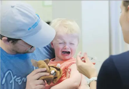  ?? GAVIN YOUNG ?? Brett Ardicl holds his son Isaac for a flu shot at the South Health Calgary Health Centre on the first day of immunizati­on clinics.