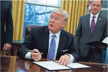  ?? EVAN VUCCI, AP ?? President Trump signs a presidenti­al memorandum to withdraw the United States from the 12-nation Trans-Pacific Partnershi­p trade pact Monday in the Oval Office.