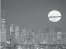  ?? AP ?? The moon rises through clouds over the skyline of lower Manhattan in this view from West Orange on Tuesday.