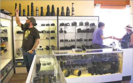 ?? JOHN GASTALDO PHOTOS ?? Camera Exposure & Safelight Labs co-owner Rob Cowan points out the camera assortment in the North Park store while Diego Jimenez helps a customer. The shop at Adams Avenue and Oregon Street also sells film, lenses, flash attachment­s and cases.
