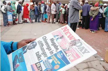  ??  ?? A man reads a newspaper as residents queue to draw money at a bank in Harare, Zimbabwe. — Reuters photo