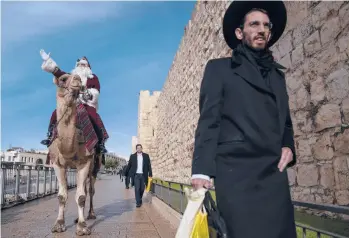  ?? ODED BALILTY/AP ?? Dressed as Santa Claus and atop a camel, Issa Kassissieh is seen Thursday outside Jerusalem’s Old City walls. Israel is considerin­g whether to approve a fourth COVID-19 vaccine dose for vulnerable people to contain the omicron variant. That comes amid debate among scientists and a lack evidence either for or against another booster.