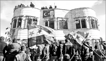  ??  ?? A banner bearing the Turkish flag and a picture of Erdogan is seen hanging from a building while Syrians wave rebel flags during a demonstrat­ion below in the rebel-held town of Azaz in northern Syria in support of a joint rebel and Turkish military...