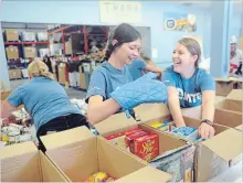  ?? DAVID BEBEE WATERLOO REGION RECORD ?? MTE Cans team members Chelsea Heibert, middle, and Alesha Collins laugh at Heibert's oven glove during the Great Food Sort Challenge at the Food Bank of Waterloo Region. Team members using an oven glove was part of the challenge for 28 teams competing to see who can sort the most food the fastest on Wednesday.