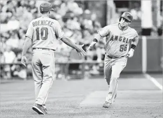  ?? Justin Berl Getty Images ?? KOLE CALHOUN of the Angels is greeted by third base coach Ron Roenicke after hitting a solo home run in the fourth inning against Pittsburgh on Friday. The Angels won, 9-2.