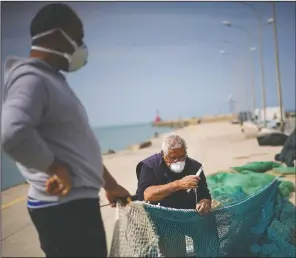  ??  ?? An elderly man repairs a fishing net as an assistant holds up the net on the empty dock of Fiumicino fishing port.