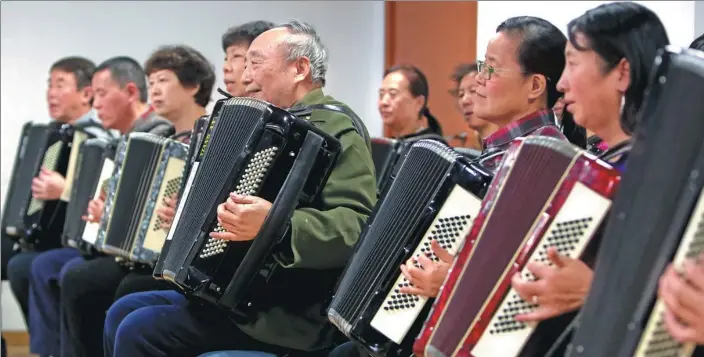  ??  ?? In a classroom on the fifth floor of China Braille Library in Beijing, accordioni­st Ren Shirong (in green coat) and his blind students play the ensemble Shepherd Girl.