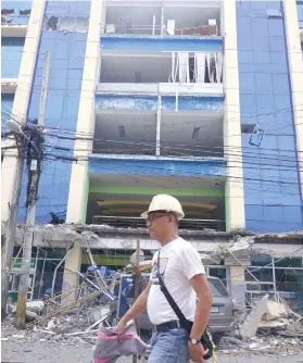  ?? AP FOTO ?? DAMAGED. A man walks past a damaged building following a powerful earthquake that shook Surigao City. Damage in infrastruc­ture is estimated at P5 million.