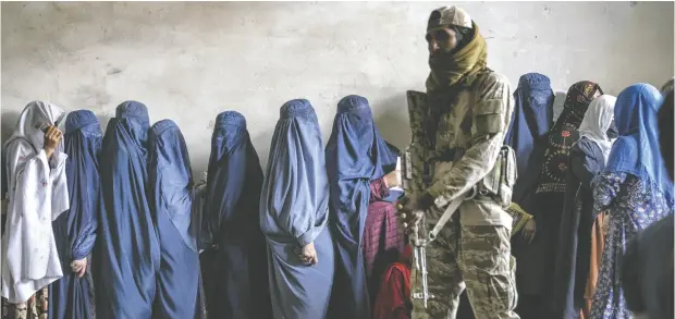  ?? EBRAHIM NOROOZI / THE ASSOCIATED PRESS FILES ?? A Taliban fighter stands guard as women wait to receive food rations distribute­d by a humanitari­an aid group in Kabul last year.