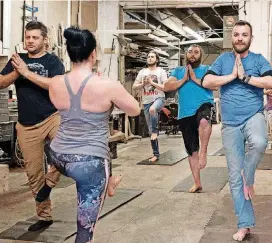  ??  ?? Woodworker Ben Dragoo, right, holds a pose during Blue Collar Yoga. It’s not unusual to see participan­ts wearing jeans and T-shirts in the class.